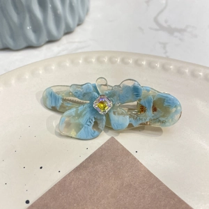 Dettaglio di un fermaglio per capelli a fiore in resina blu con cristallo su un piatto