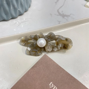 Macro detail of marble resin butterfly clip with white pearl and golden spring