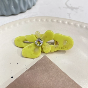Dettaglio del fermaglio per capelli a fiore in acetato giallo con gemma colorata