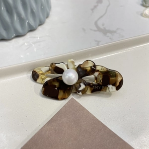 Close-up of tortoise acetate flower hair clip with a large pearl and brand logo engraving