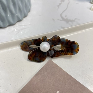 Macro detail of tortoiseshell acetate flower hair clip with a large white pearl center