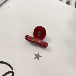 Gros plan d'une pince à cheveux en résine rouge vin brillant avec lettrage doré chic