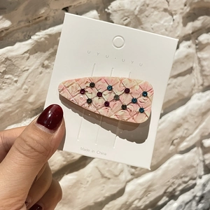 Détail d'une pince à cheveux en acétate rose marbré avec strass sur support blanc