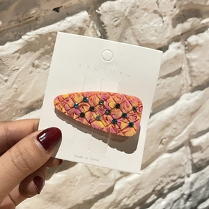 Détail d'une pince à cheveux en acétate avec motif marbré et strass colorés sur carte de support