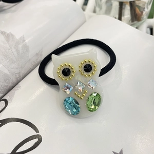 Detail eines Eulen-Haargummis mit bunten Kunstkristallen auf schwarzem Gummiband