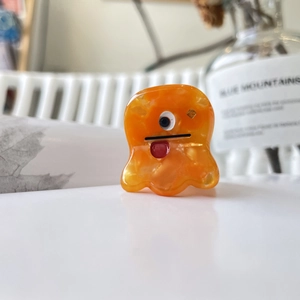 Vue détaillée d'une pince à cheveux monstre en acétate orange marbré avec un œil décalé