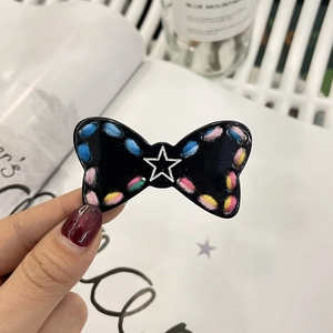 Detail of a fuzzy black bow hair clip with colorful stitching and a silver star center