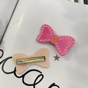 Detail of pink and beige bow hair clips with pearls, star patterns and gold duckbill clips