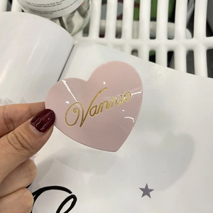 Dettaglio del fermaglio a cuore rosa con scritta Vannie dorata tenuto in mano