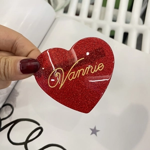 Dettaglio ravvicinato della molletta a cuore con glitter rossi e scritta dorata Vannie
