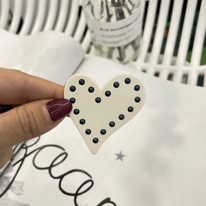 Vue détaillée de la pince à cheveux en forme de cœur crème avec perles à pois noirs