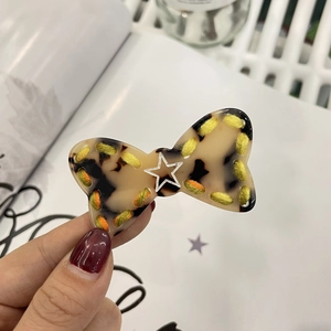 Close-up of tortoise shell bow hair clip with colorful stitching and a white star