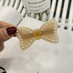 Close-up of a khaki bow hair clip with white pearls and a yellow star detail