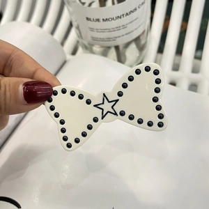 Detail of a Y2K style white bow hair clip with black star pattern and pearl trim