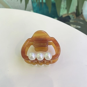 Elegant amber acetate hair claw clip with large iridescent pearls and gold brand detail