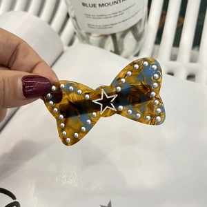 Detailed close-up of a tortoiseshell bow hair clip with pearls and silver star detail
