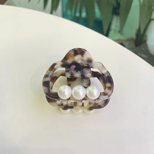 Close-up of tortoise shell acetate hair claw clip with pearl accents and gold logo