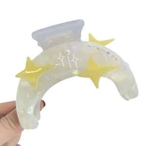 Pinza per capelli in acetato bianco con stelle gialle e strass tenuta in mano