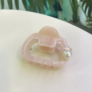 Pince à cheveux rose en acétate avec perle brillante et strass sur un bureau blanc