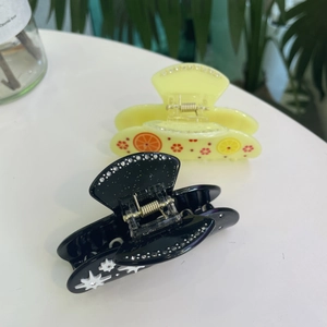 Detail of star-patterned black hair claw and lemon-print acetate clip with metal spring