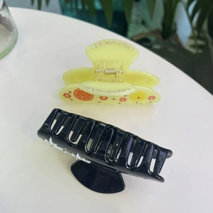 Detail of yellow acetate hair claw with fruit print and black clip with glitter finish
