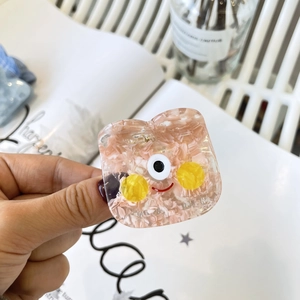 Détail d'une mini pince à cheveux monstre en acétate rose avec un visage cartoon y2k