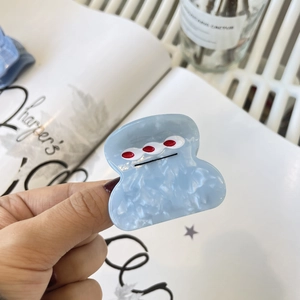 Gros plan sur une pince à cheveux bleue en acétate marbré avec motif monstre rigolo