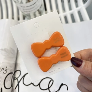 Elegant pair of bright orange bow-shaped hair clips displayed on a white branded card