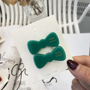 Detail of dark green handmade bow hair clips with gold lettering on a white display card