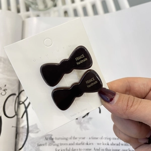 Close-up of two wine red bow hair clips with gold lettering on display card
