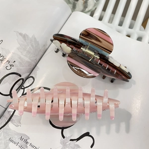 Dettaglio di due mollette in acetato con strisce rosa e accenti perlati su una rivista