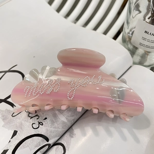 Dettaglio della molletta in acetato rosa con scritte in perle e trama a strisce