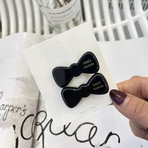 Detail of two black bow-shaped resin hair clips with golden handmade text on card