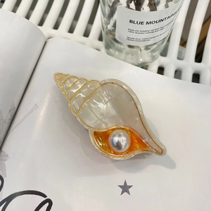 Gros plan sur pince à cheveux en acétate en forme de coquillage avec perle décorative