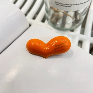 Nahaufnahme der glänzend orangefarbenen Haarspange in Herzform mit Goldlogo