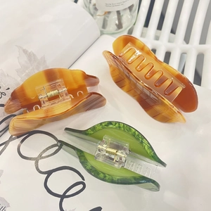 Detailed view of leaf-shaped acetate hair claws in amber and green resin material