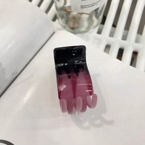 Detailed view of a small black and purple gradient hair claw clip on a white book surface