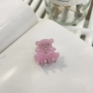 Détail d'une pince à cheveux ours rose en acétate avec strass sur une page de livre