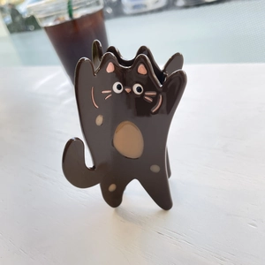 Détail d'une mignonne pince à cheveux chat noir en acétate sur une table en bois blanc