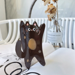 Pince à cheveux chat marron en acétate avec pois crème posée sur un livre ouvert