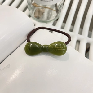 Détail d'un élastique à cheveux en résine vert foncé avec lettrage doré sur fond blanc