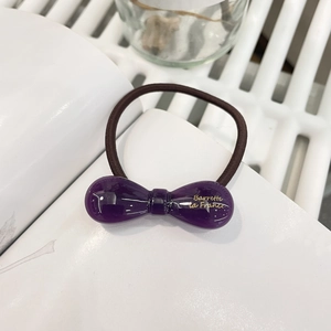 Détail d'un chouchou noeud en résine violette avec lettrage doré et élastique marron