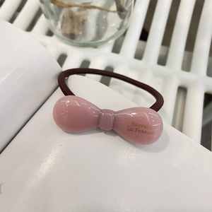Détail d'un élastique à cheveux rose avec nœud en résine et lettrage doré Barrette La France