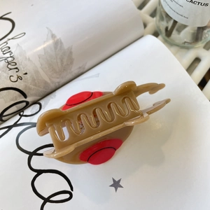 Dettaglio della pinza per capelli in acetato marrone con accenti rossi su rivista