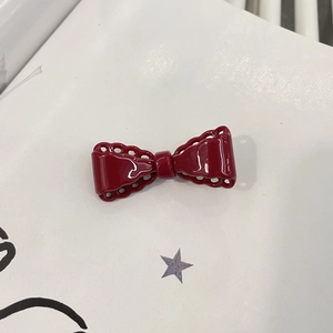 Retro red bow hair clip with gold logo and wavy cut-out edges on a white background