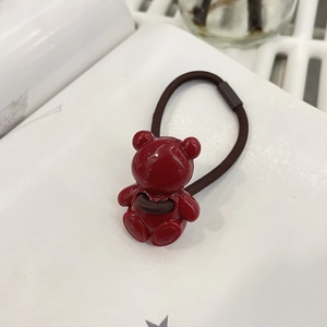 Close-up of a glossy red bear charm on a dark brown elastic hair tie for kids