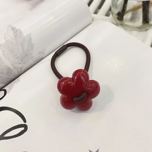Close-up of a glossy red flower hair clip on a white magazine with artful shadows
