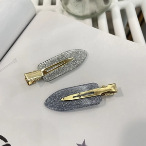 Nahaufnahme von Glitzer-Haarspangen in Silber und Blaugrau mit goldener Entenschnabelbasis