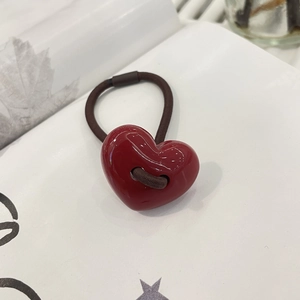 Detail view of a glossy red heart charm with brown elastic hair tie on a white page