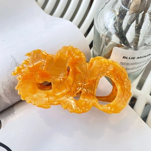 Elegant dragon-shaped amber acetate hair claw clip on a white book with decor